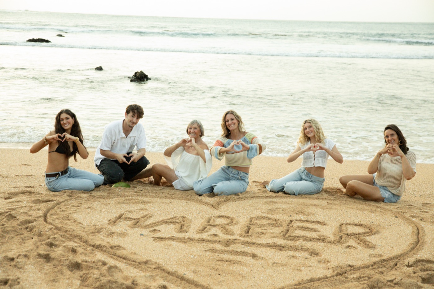 Family sitting on a Hawaii beach around HARPER written in a heart in the sand
